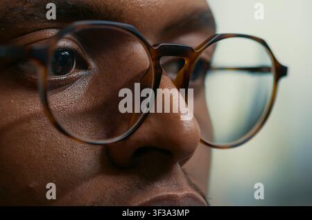 Concentrated close portrait with african american database developer with glasses working concentrated reviewing computer screen at a computer screen, showing software development focus, coding. Stock Photo
