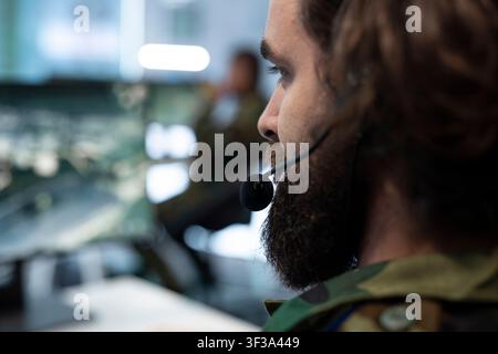 Close up of military operator wearing communications headset while watching command center activity. Army dispatcher listens to radio communication to follows operation updates Stock Photo