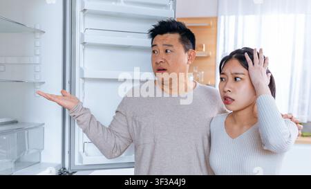 Worried Asian Couple Looking Inside Empty Refrigerator In Modern Kitchen, Food Shortage Concept Stock Photo
