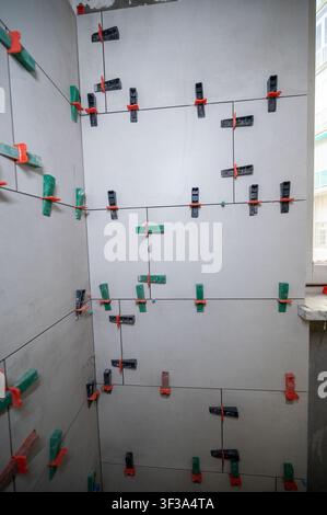 Walls with ceramic tiles featuring leveling clips and spacers, ensuring precise alignment and consistent grout lines during a home renovation project Stock Photo