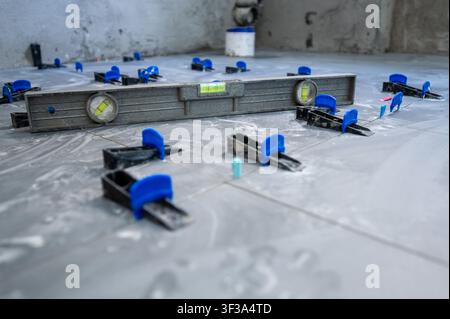 Tiler installing new ceramic floor tiles with a tile leveling system, ensuring even surfaces for house renovation work on a construction site Stock Photo