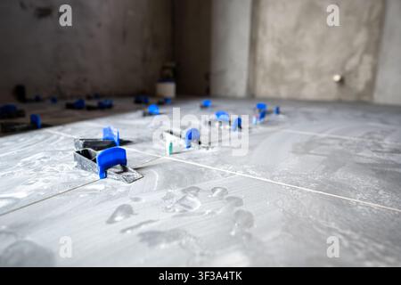 Grey floor tiles installing in a new house or apartment, showing clips and wedges of a tile leveling system ensuring an even surface during the renova Stock Photo
