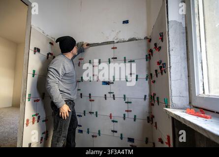Professional tiler ensuring a perfect level on bathroom wall tiles using a spirit level and tile leveling system, performing house renovation work Stock Photo
