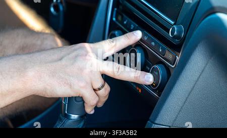 Close up of a driver hand adjusting climate control and air conditioning in a modern car. Vehicle dashboard with temperature controls and infotainment Stock Photo