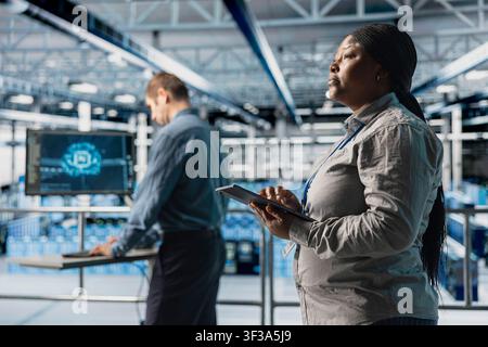 Teamworking data center system administrators review code for AI automation scripts. Server room colleagues run artificial intelligence assisted diagnostics on equipment for predictive error detection Stock Photo