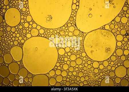 Oil and water mixing, forming abstract golden bubbles and patterns on a liquid surface Stock Photo