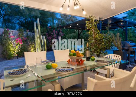 A beautifully set outdoor dining table evening under a covered patio. Lush greenery and a relaxed atmosphere. Stock Photo