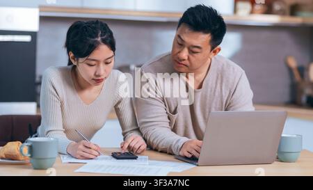 Focused Asian Woman Working With Calculator And Asian Man Observing At Home Office, Business Concept Stock Photo