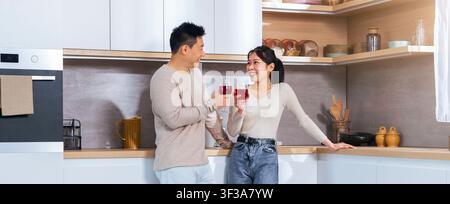 Happy Asian Couple Toasting Drinks In Modern Kitchen, Celebrating Special Moment Together Stock Photo