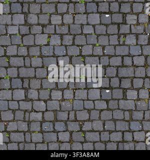Overhead top view of dark grey square basalt cobblestone pavement setts with small green weeds growing in the joints. Stock Photo