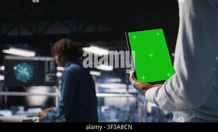 Data center worker using green screen mockup tablet, doing maintenance on rigs handling AI tasks. Server hub admin using chroma key device to manage storage arrays supporting deep learning, Stock Photo
