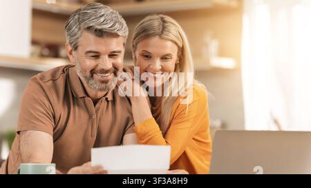 Happy Caucasian Couple Smiling Together While Looking At Documents In Kitchen, Home Concept Stock Photo