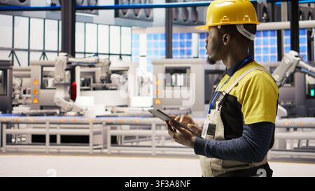 Engineer oversees solar panel production lines equipment using tablet app. Worker maintains photovoltaic assembly systems in automated industry 4.0 factory using digital device application, camera A Stock Photo