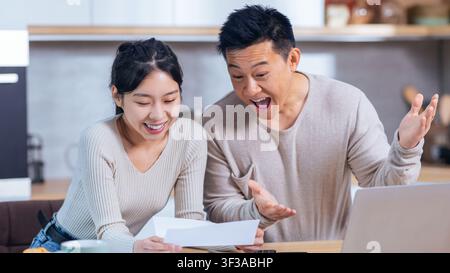 Happy Asian Couple Celebrating Success In Kitchen, Excited With News And Sharing Joy Stock Photo