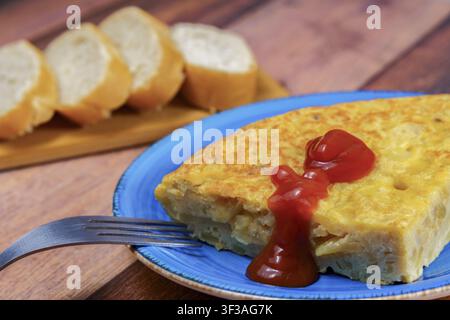 Traditional tortilla de patatas serving with a fork, ketchup, and sliced baguette for breakfast or tapas Stock Photo