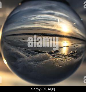 Sunset glows through a lens ball at St. Pete Beach, with seafoam and golden sun creating a dreamy coastal reflection. Stock Photo