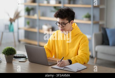 Smiling asian man working on laptop and writing Stock Photo