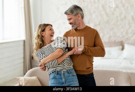 Cheerful Middle Aged Couple Dancing In Modern Bedroom At Home Stock Photo