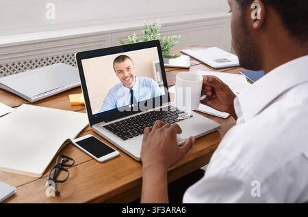 Businessman At Laptop Having Online Meeting With Coworker At Workplace Stock Photo