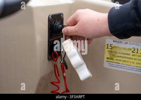 A close-up shot of a person's hand turning the ignition key on a boat console panel, with a red safety lanyard hanging below. Stock Photo