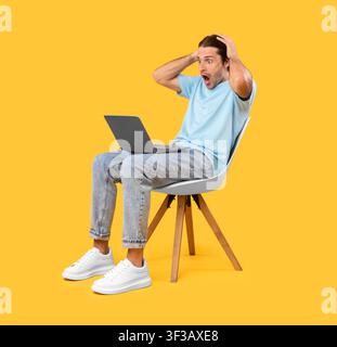 Surprised shocked guy using laptop sitting on chair Stock Photo