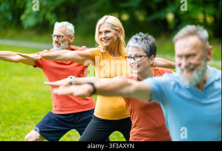 Group of senior people practicing yoga outdoors, standing in Warrior two pose Stock Photo