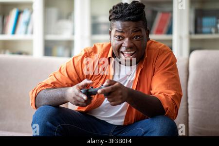 Happy young chubby black man playing video games at home Stock Photo