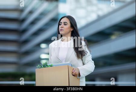 Sad business lady carrying box belongings leaving office after layoff Stock Photo