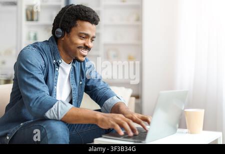 Young Black Man With Headphones Working on Laptop Indoors Stock Photo