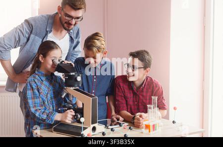 Children engaged in hands-on science experiment with microscope in classroom Stock Photo
