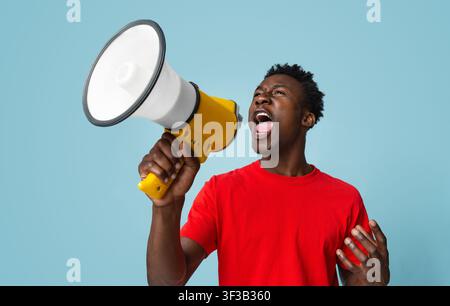 Portrait Of Emotional African American Guy Shouting With Megaphone Over Blue Background Stock Photo