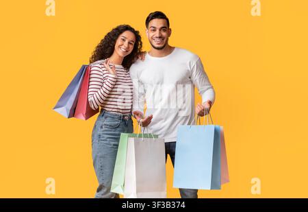 Middle Eastern Couple Posing With Shopping Bags In Hands Over Yellow Background Stock Photo