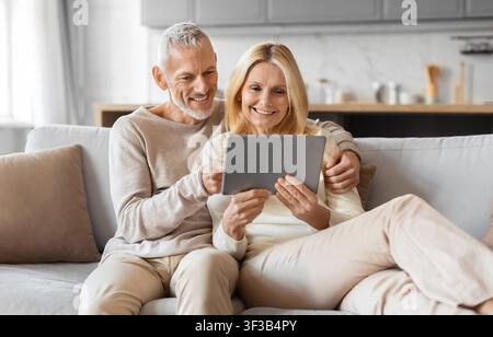 Excited smiling senior spouses using digital tablet computer at home Stock Photo