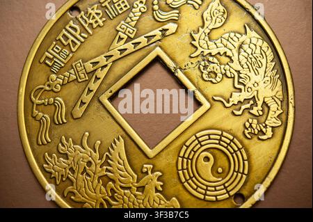 Monochrome macro of a Chinese-style coin amulet with dragon, phoenix, yin yang and a square central hole Stock Photo