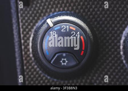 An extreme macro shot showing a circular vehicle climate control temperature dial switch with degree numbers on a dark textured carbon fiber dashboard Stock Photo