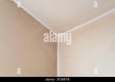 A close up detail shot showing the clean geometrical lines of an interior room corner where two beige plaster walls meet the ceiling, highlighting tex Stock Photo