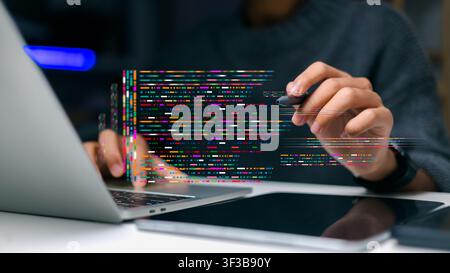 Close up programmer holding stylus pen pointing at colorful software coding script while working on laptop computer at office desk, digital applicatio Stock Photo