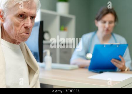 Serious senior patient waiting with concerned expression in examination room. Elderly man undergoing health assessment during routine checkup. Older gentleman being observed for preventive monitoring Stock Photo