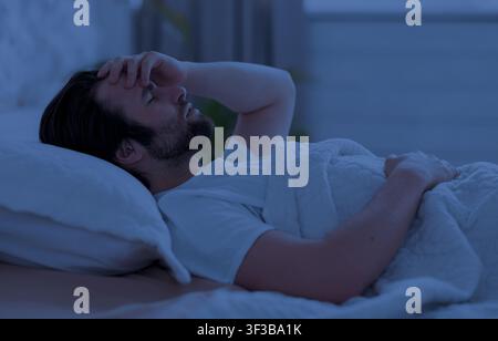 Sleepless man laying in bed alone at night Stock Photo