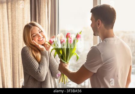 Romantic young man presenting flowers to his girlfriend at home Stock Photo