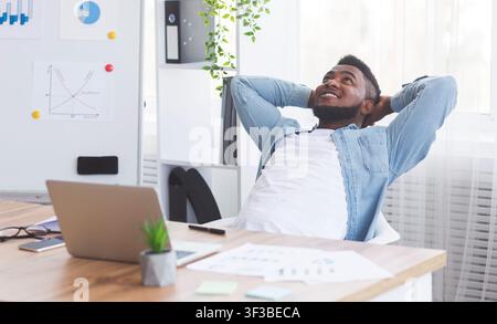 Dreamy African American employee resting at workplace with hands behind head Stock Photo