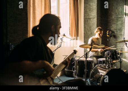 Drummer rehearsing in music studio while bassist plays in foreground, live band practice, drum kit performance, recording session, creative collaboration. Stock Photo