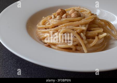 Close-up front shot of spaghettoni pasta with creamy Castelmagno cheese sauce, hazelnuts and pine nuts Stock Photo