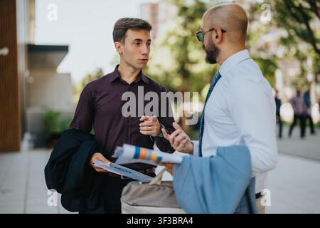 Two business colleagues having an outdoor discussion over documents near an office building Stock Photo