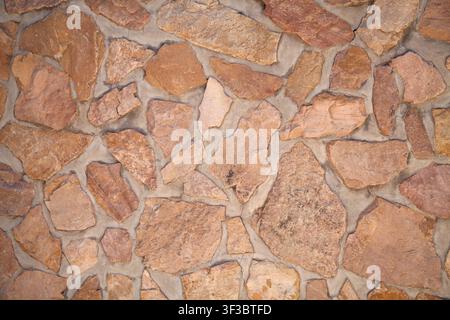 Close-up view of a rustic stone wall constructed from irregular, rough-hewn stone blocks in warm earthy tones of orange, beige, and tan. The natural s Stock Photo