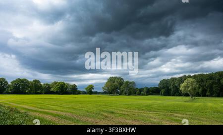 Dramatic storm clouds gathering above green farmland and trees, capturing the approach of severe weather across the countryside Stock Photo