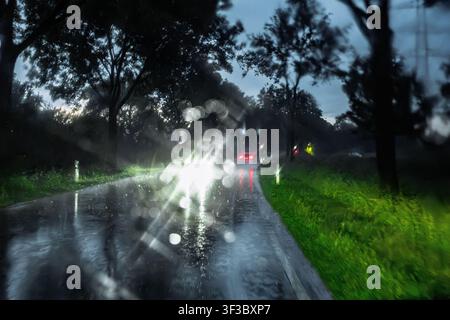 Cars driving through heavy rain on a wet road during a stormy evening, viewed through a windshield covered with raindrops Stock Photo