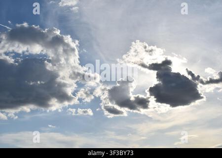 Dramatic dark clouds with sun shining from behind against a blue sky Stock Photo