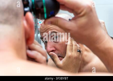 Man shaving head with electric razor in mirror Stock Photo