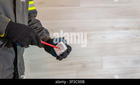 Electrician repairing electrical socket with screwdriver, male hands in protective gloves fixing wall outlet during home repair work. Electrical maint Stock Photo